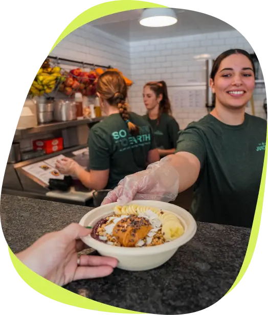 Team member handing a fresh smoothie bowl across the counter to a customer at The Juicery.